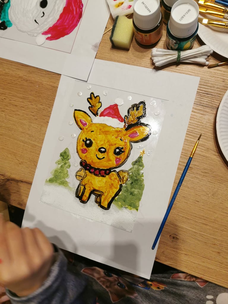 Hand-drawn artwork of a cute yellow deer wearing a Santa hat with pink accents and green foliage background on white paper