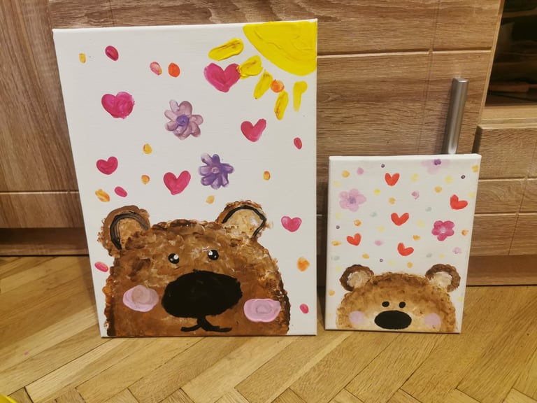 Two canvas paintings with cute brown bears and colorful hearts, flowers, and sun designs on wooden floor