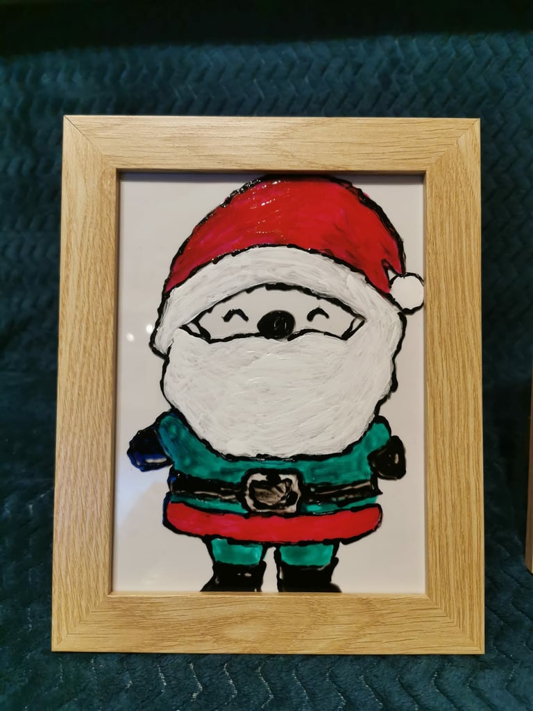 Simple painted illustration of Santa Claus with a red hat and white beard, wearing a green and red outfit, framed in light wood