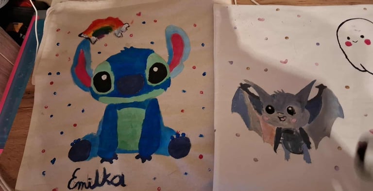Two childrens drawings: a blue alien character with large eyes and red antennae labeled Comilka, and a small gray bat character on a polka dot background