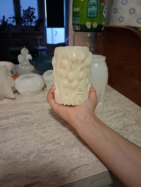 Person holding a white decorative candle with leaf and spiral designs on a kitchen counter