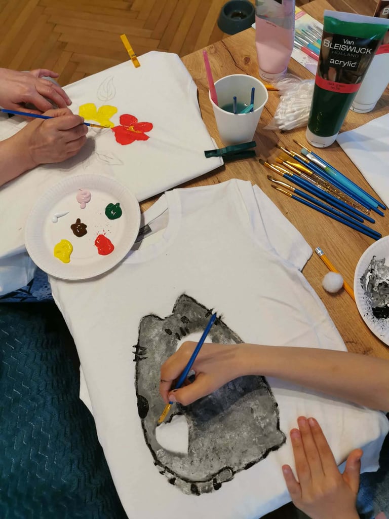 Two children painting at a wooden table with brushes, colorful acrylic paints, and white canvas paper